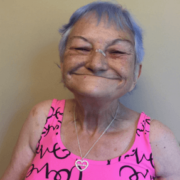 Woman with pink tank top, heart neckless, and purple hair grinning at camera